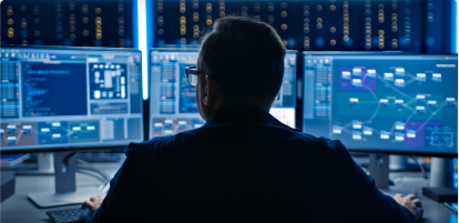 A cyber security professional seen from his back with 3 screens in front of him.